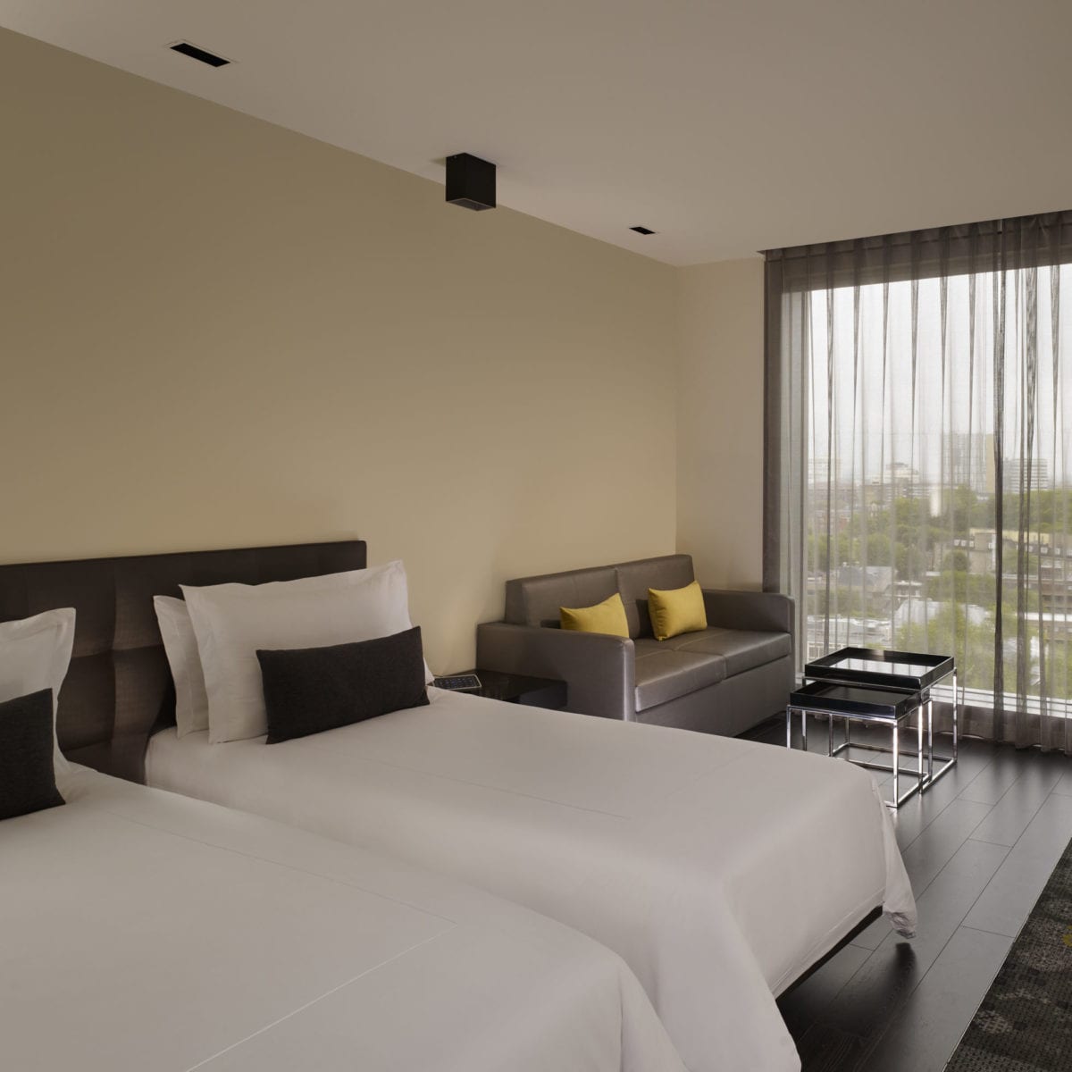 Picture of twin beds with a brown sofa, a desk and two small tables behind it.