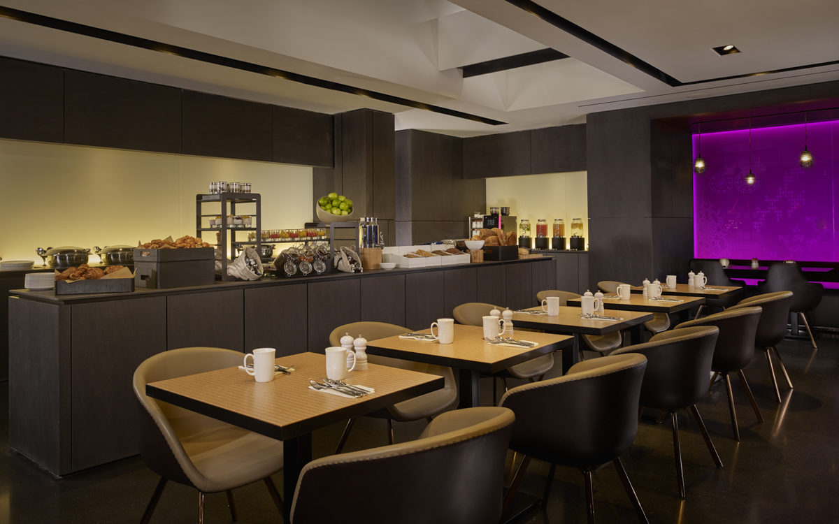 Brown tables and brown chairs set-up in a spacious breakfast room with a purple light in the background