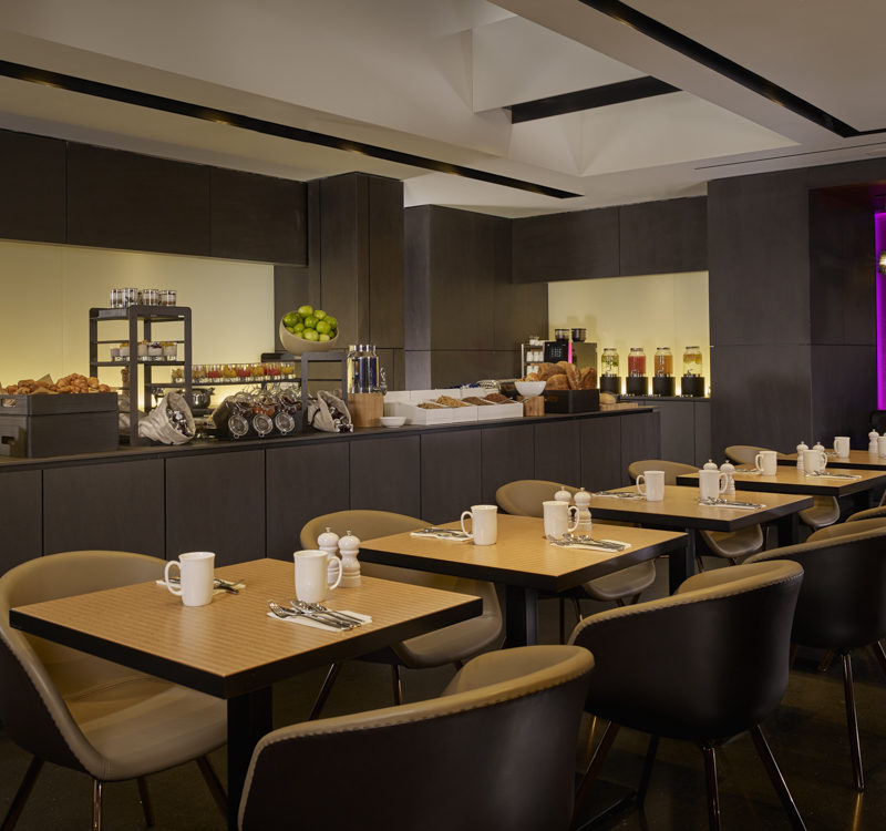 Brown tables and brown chairs set-up in a spacious breakfast room with a purple light in the background