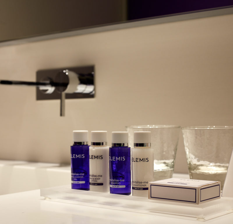 Bathroom amenities consisting of white and blue bottles in front of two crystal clear glasses