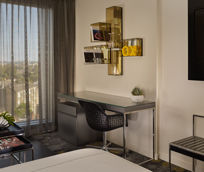 A grey desk in a studio room with a gold shelf modern shelf above it