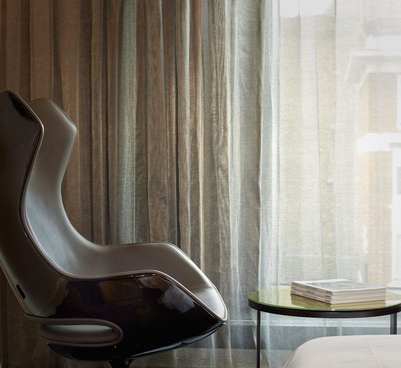 A brown curved chair in front of a small table that hold a book