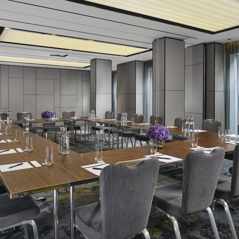 Brown tables in a circular set up with grey chairs all the way along and purple flowers on the tables