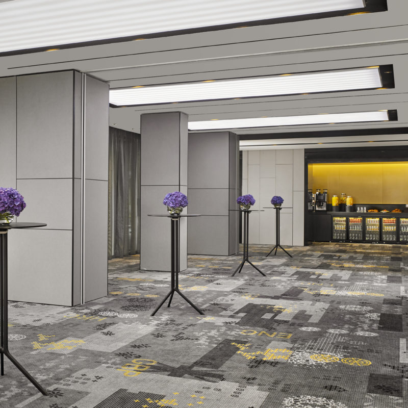 Small tables with purple flowers on top of them lead down to a room full of fridges with yellow lighting