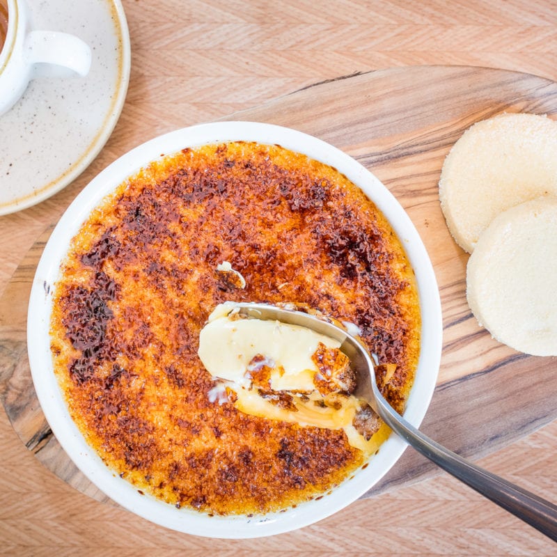 An aerial shot of a spoon cracking the hard top of a creme brulee revealing a soft custard interior