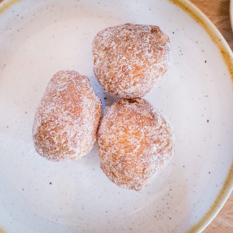 three filled Venetian style donuts covered in white icing sugar