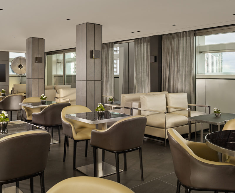 A room full of yellow and brown chairs and grey tables with beige sofas in the background in the Executive Lounge at Park Plaza London Waterloo