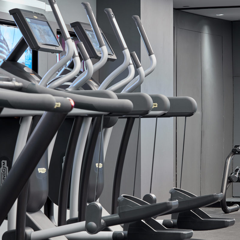 A row of silver metal running machines with blue screens on them