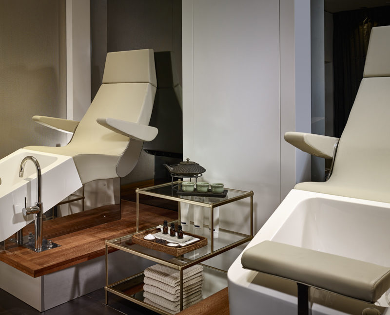 Two beige manicure and pedicure chairs with a small table in the middle
