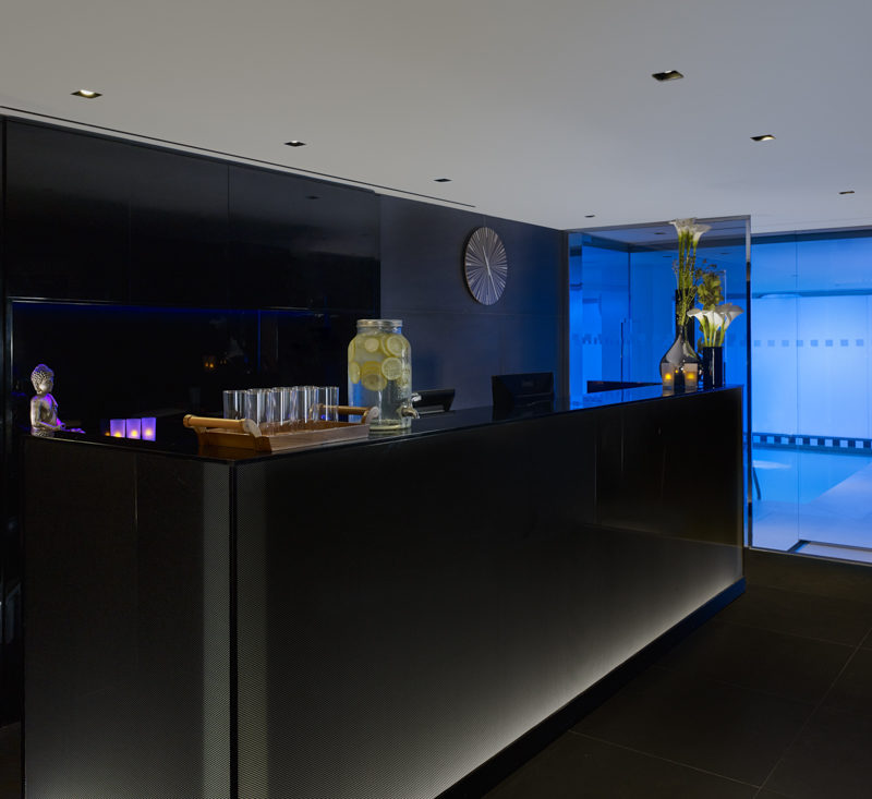 The large black front desk of the spa with the bright blue pool in the background