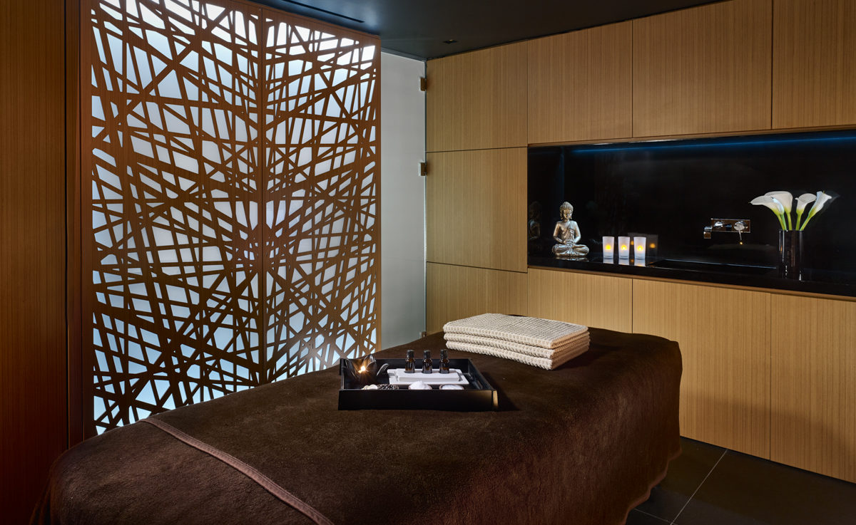 A brown massage bed with treatment equipment on it and a silver buddha in the background