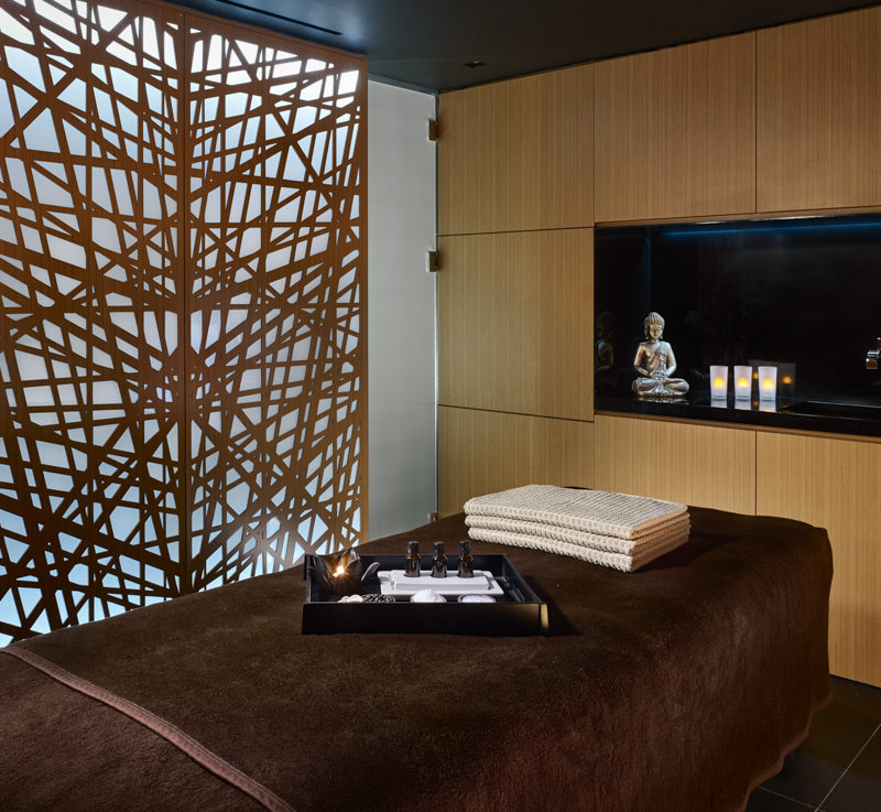 A brown massage bed with treatment equipment on it and a silver buddha in the background