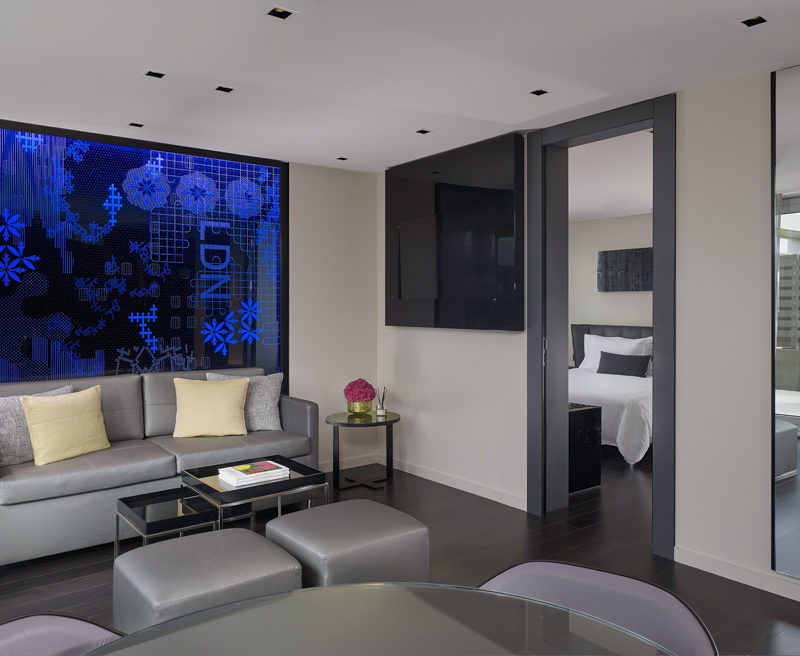 A large room with a grey dining table and chairs and a grey sofa in front of a blue lit wall