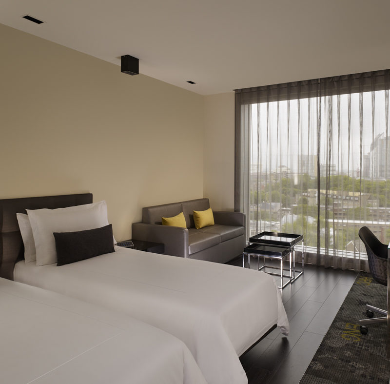 Bright white twin beds in front of a sofa with yellow pillows