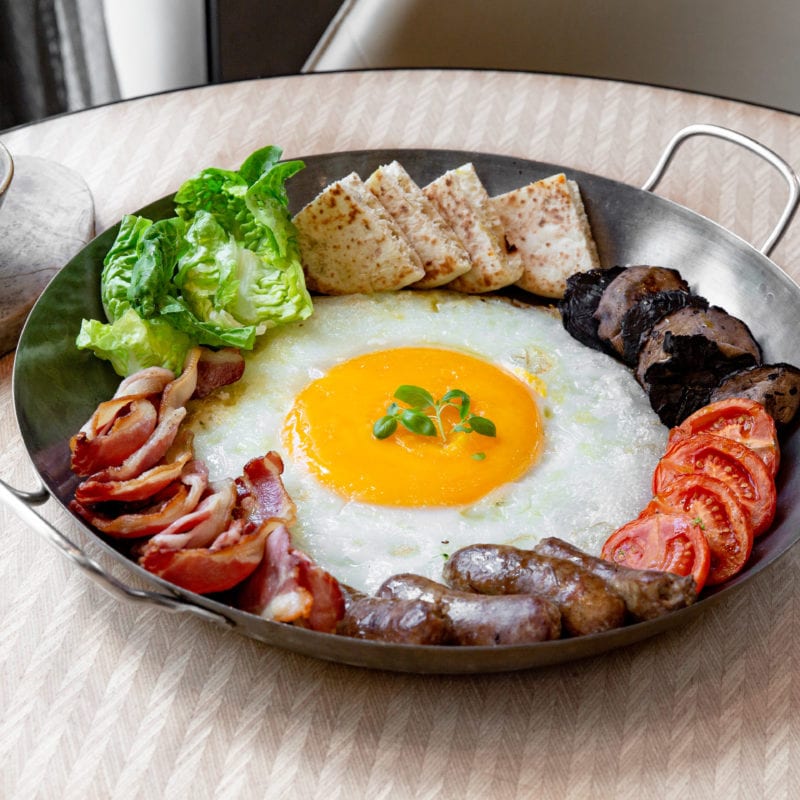 The Ostrich Egg Full English Breakfast comes with fried tomatoes, portobello mushrooms, streaky bacon, baked beans, sourdough bread, and Cumberland sausages.