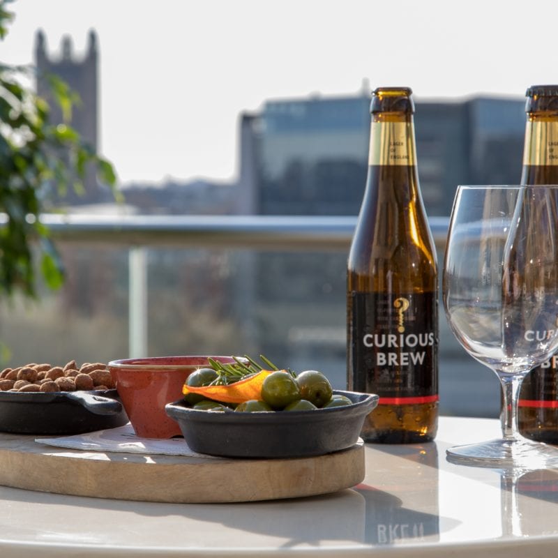 A tray of brown nuts and bright green olives in front of two brown bottles of beer