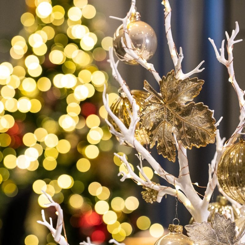 A white tree in focus with gold baubles on it