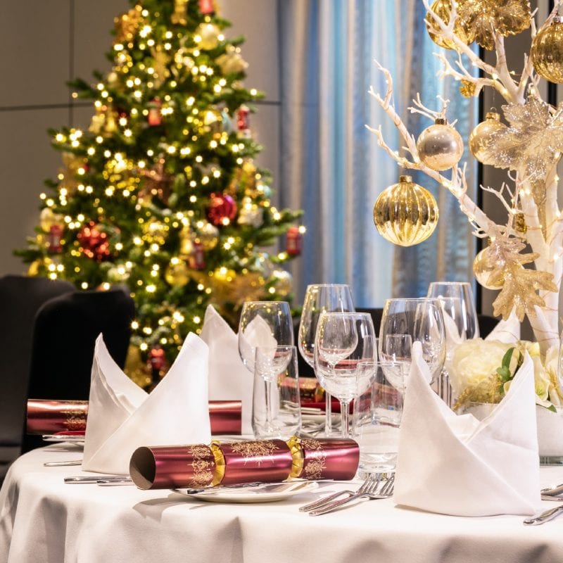Bright red crackers on a pristine white table with a white tree and gold baubles